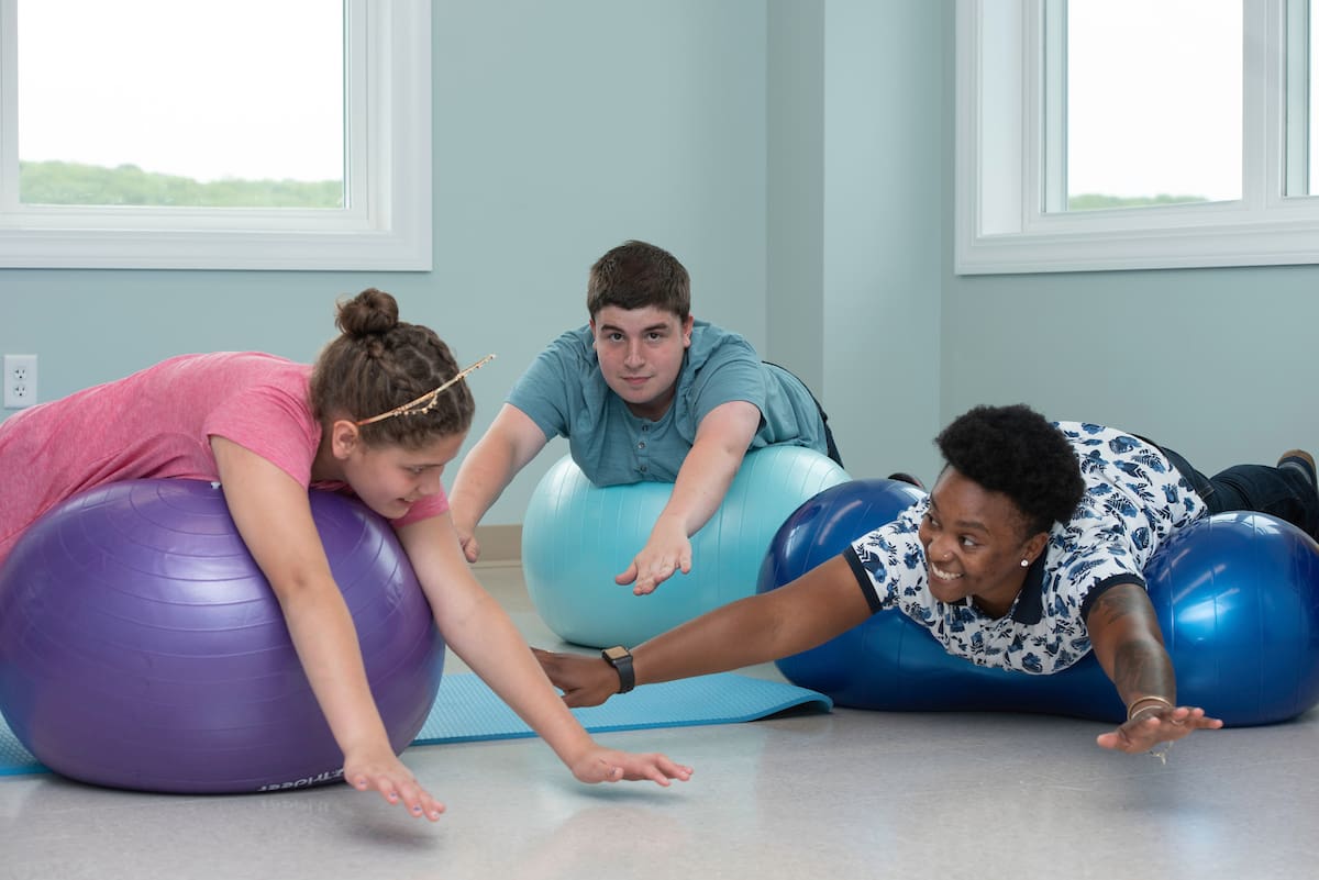 Three individuals practicing physical therapy or stretching with exercise balls in a room.
