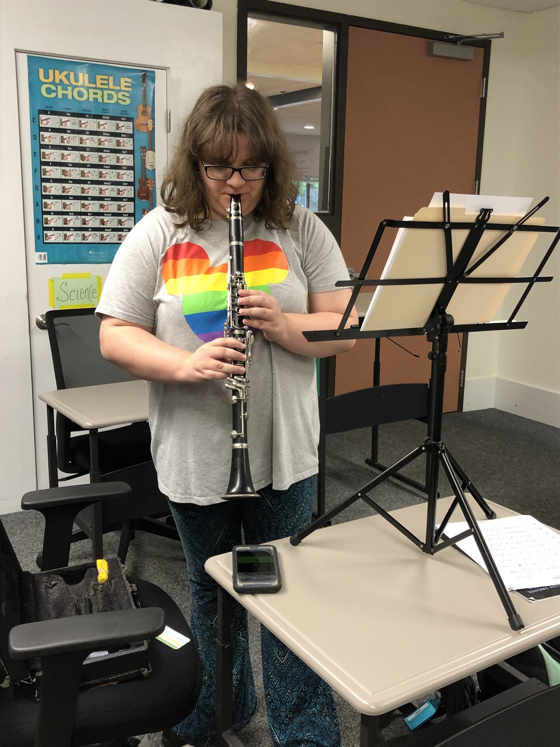 Student playing a clarinet with sheet music on a stand in a room with charts and signs.