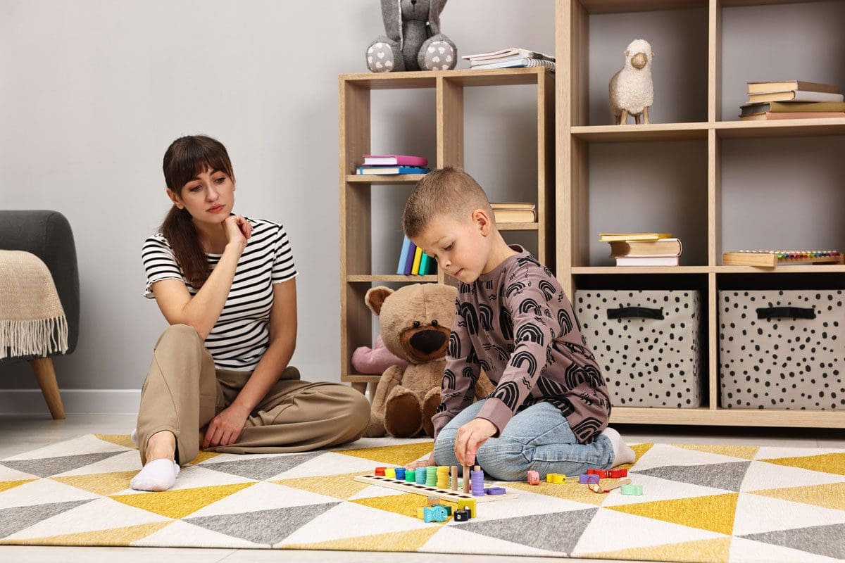 Adult supervising a child engaged in a learning activity with blocks in a playroom.