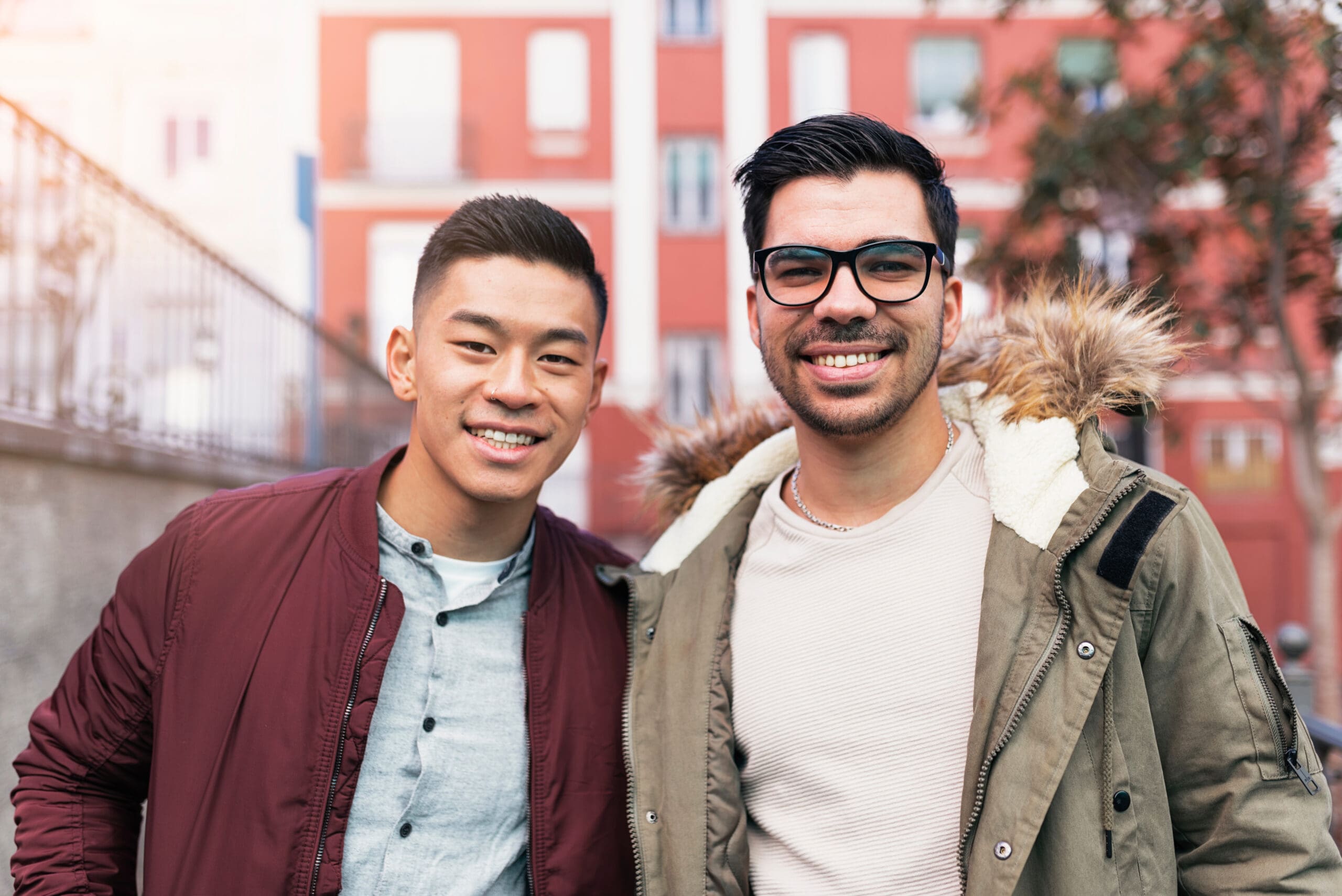 Two smiling individuals outdoors, one wearing glasses and a fur-lined jacket.