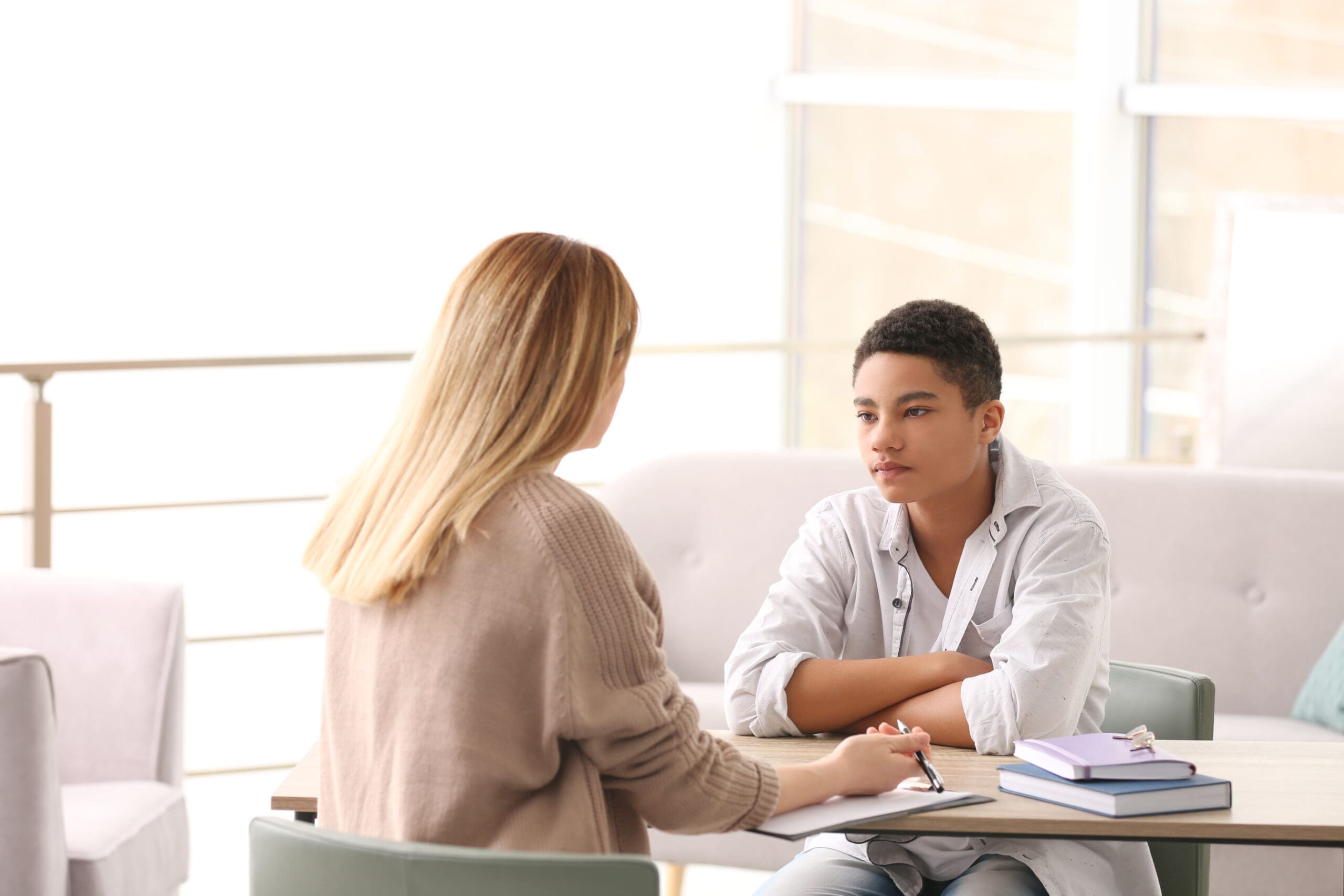 A person with long blonde hair speaking to a young person with short black hair in a counseling setting