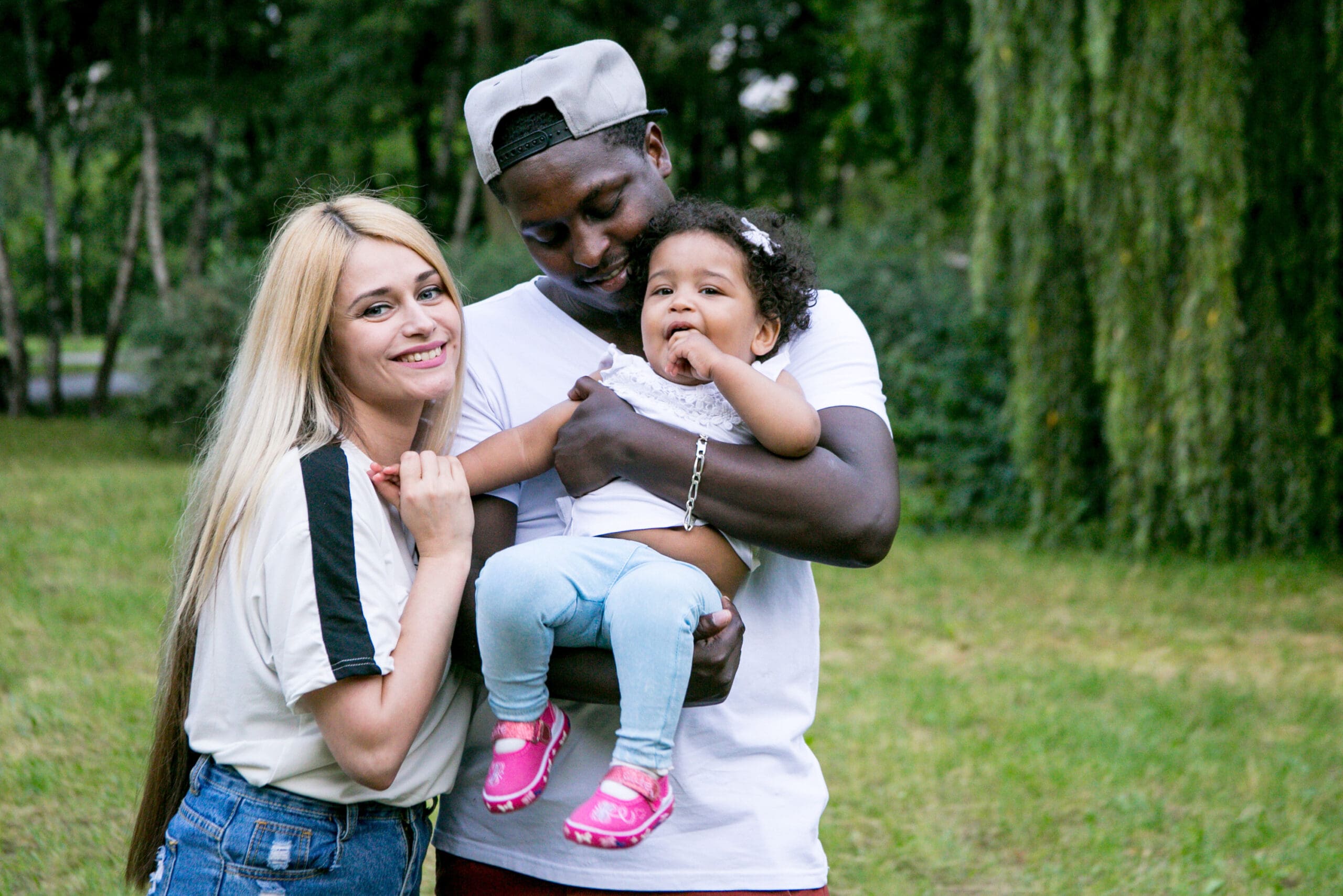 Family of three with a young daughter smiling in a park.