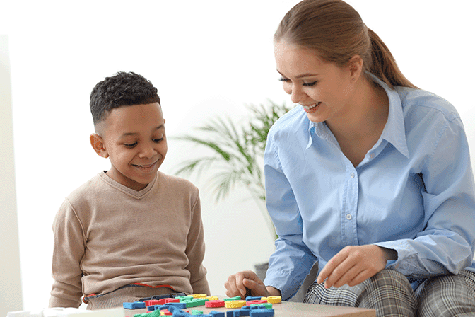 A woman and a young boy playing with colorful toy blocks on a table.