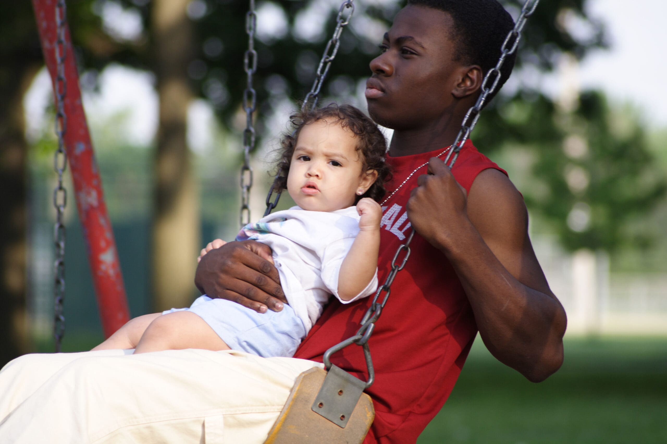 Man sitting on a swing holding a toddler.