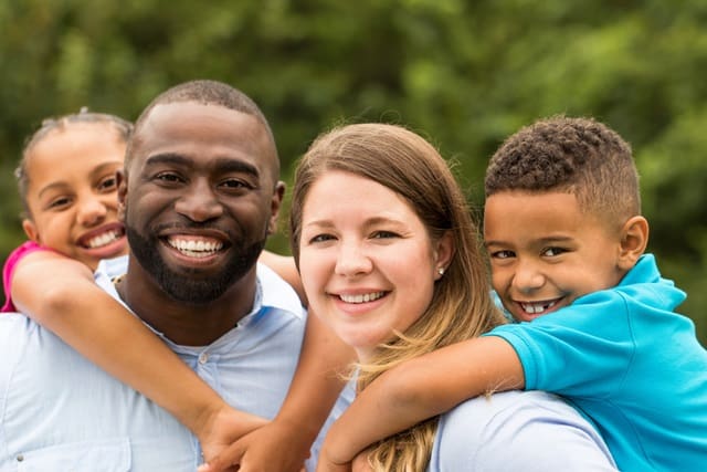 Group of smiling family of four, with children hugging parents.