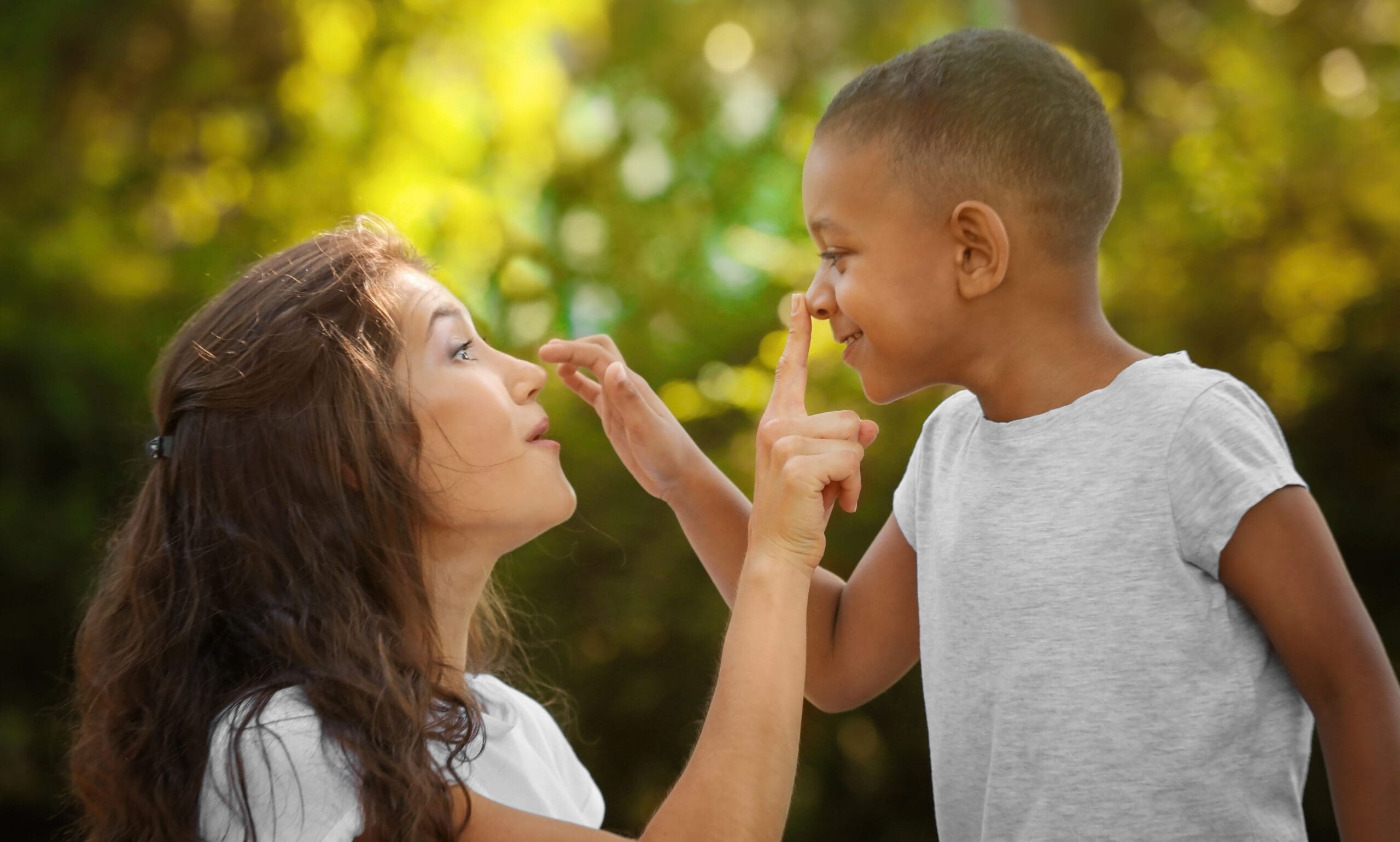Caregiver and child smiling at each other outdoors.