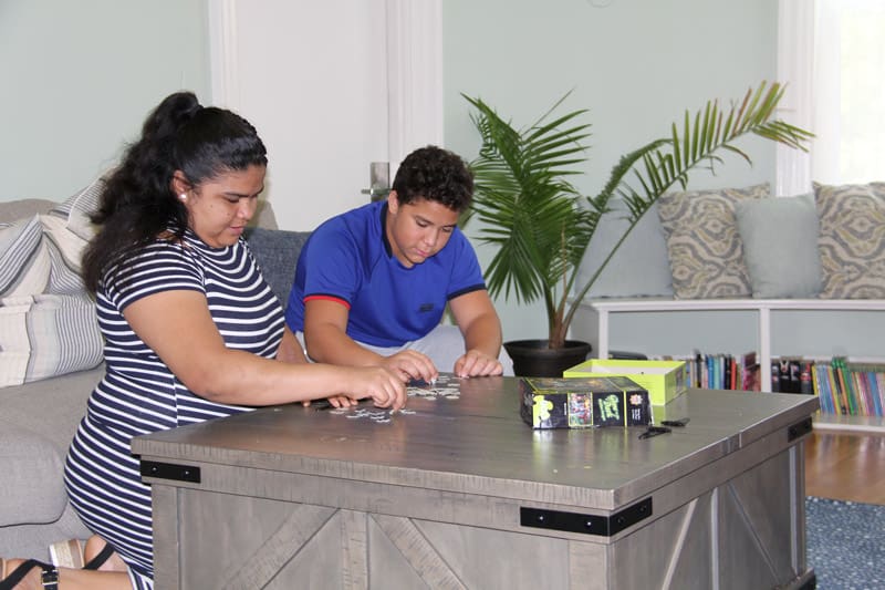 Two teenagers playing a puzzle on a table in a living room.
