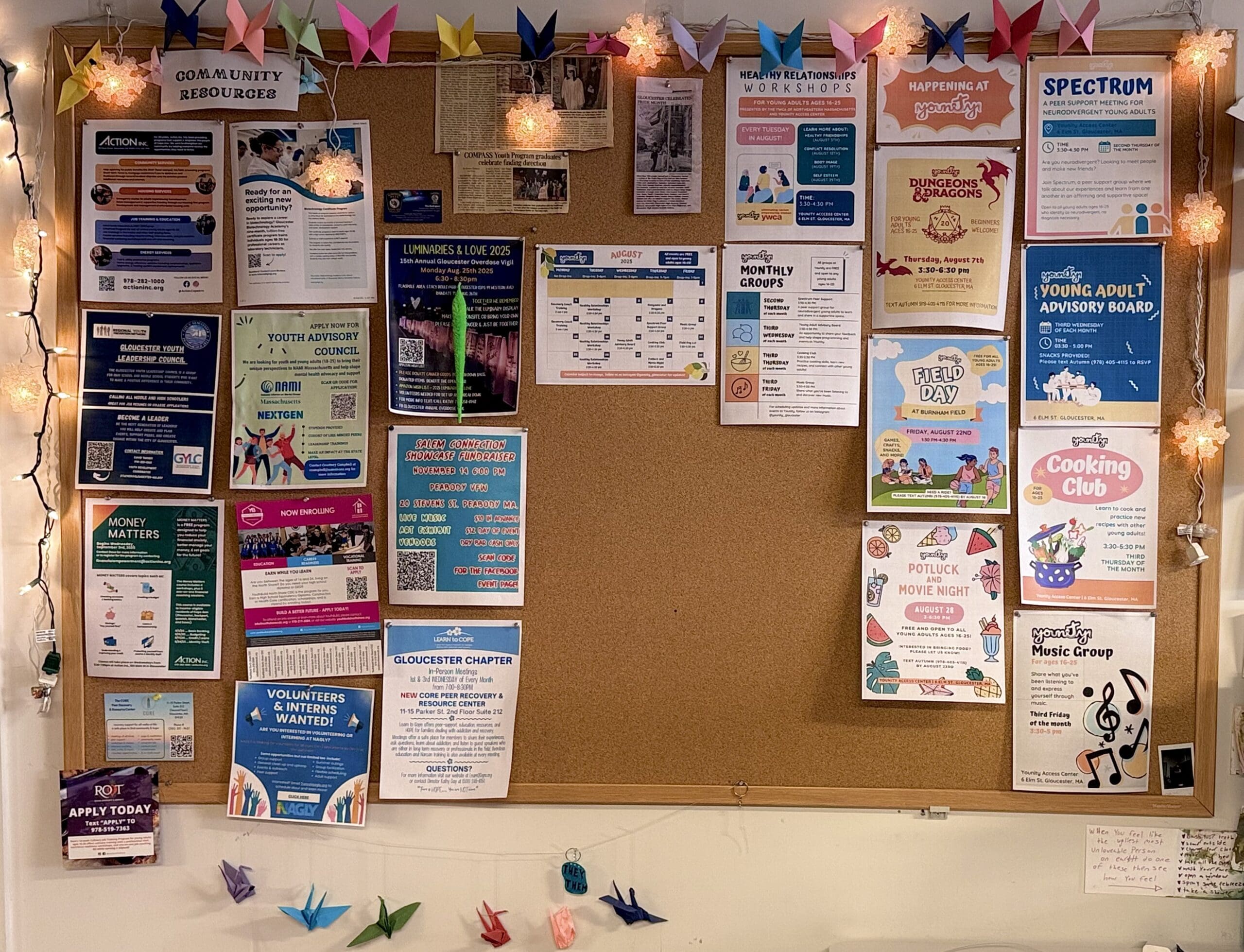 Bulletin board with community event posters, flyers, and decorations, decorated with string lights and origami cranes.