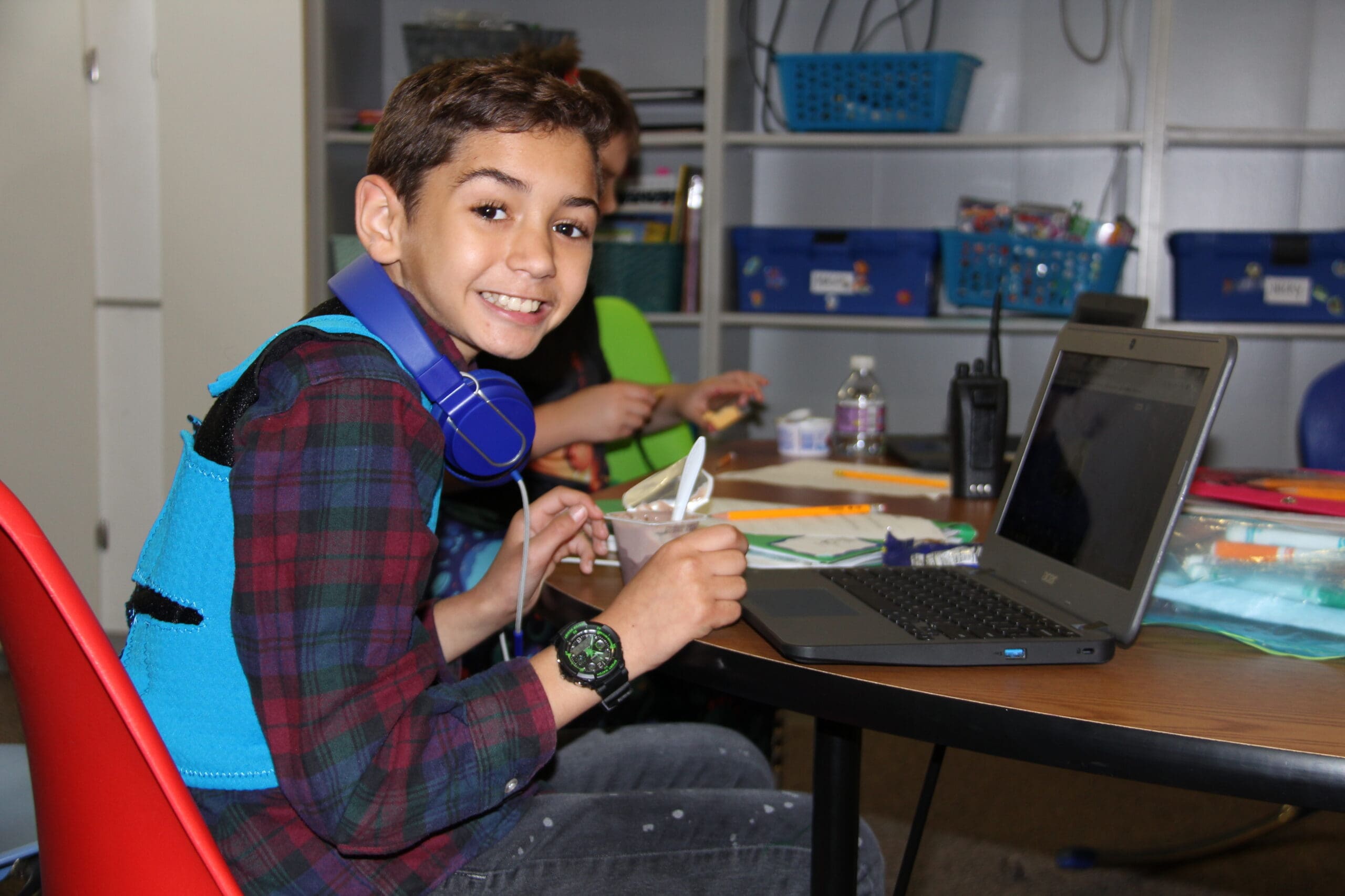 Littleton student with headphones sitting at a table with a laptop and a bowl of food, smiling.