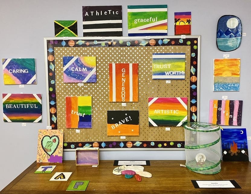 Display of colorful paintings with words like 'Caring,' 'Calm,' 'Generous,' and 'Trustworthy'.
