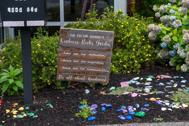 Garden at The Victor School with painted rocks and a sign promoting kindness and inspiration.