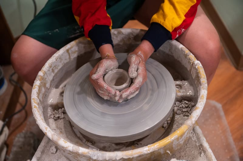 Person shaping clay on a pottery wheel with hands covered in clay