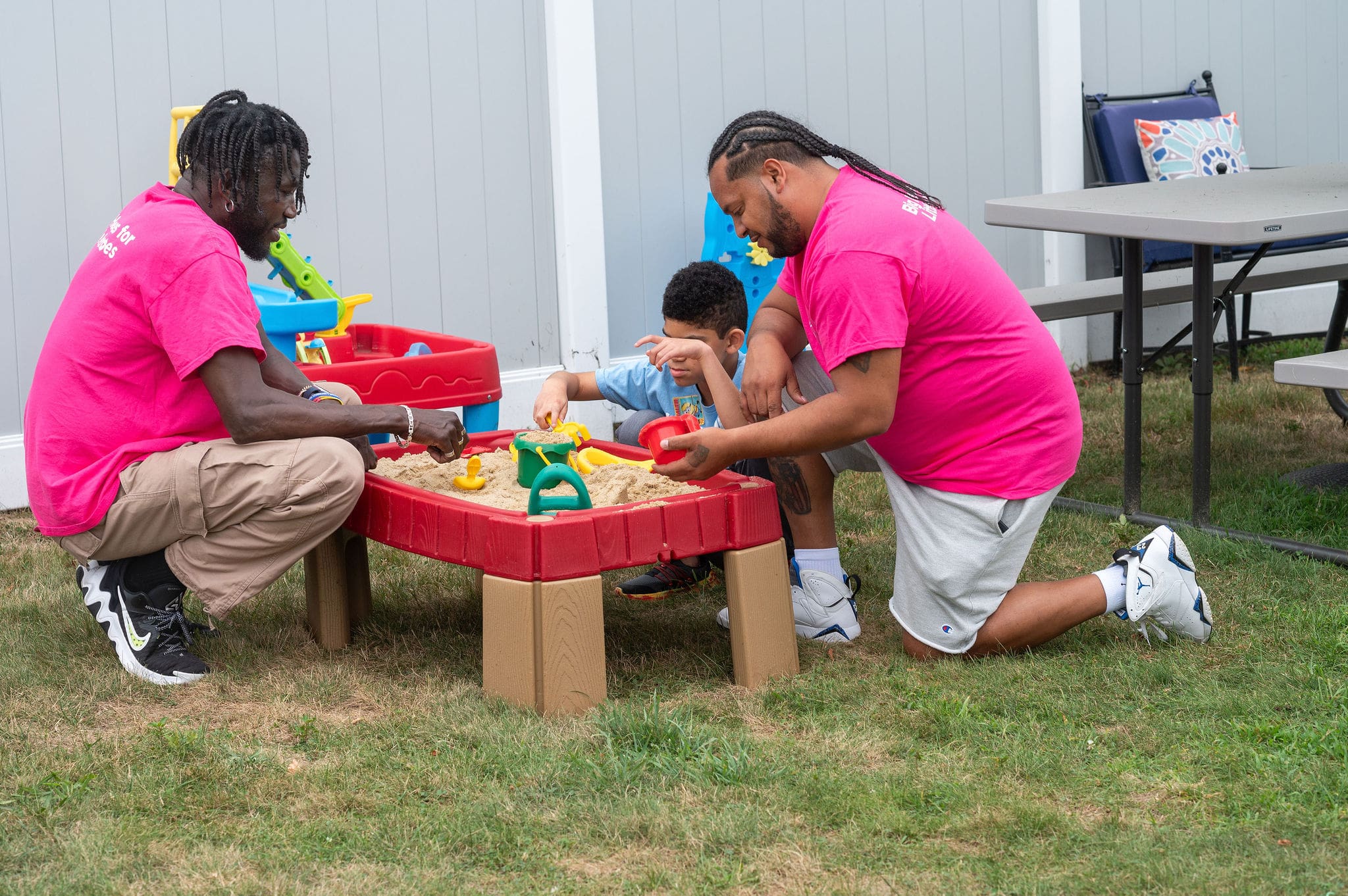 Two men and a boy playing in a sandbox outdoors.