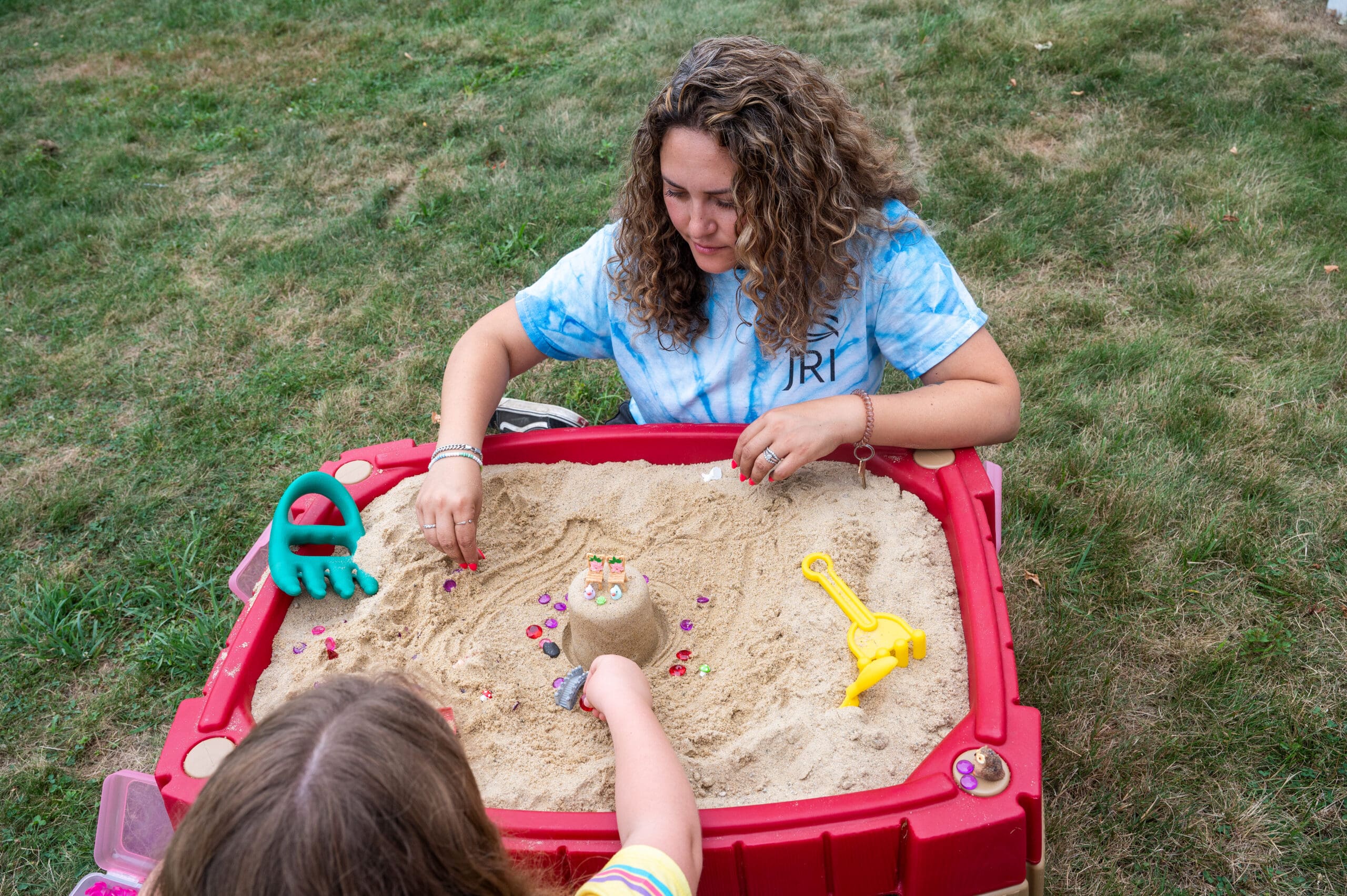Woman and child playing in a sandpit with toys outdoors.