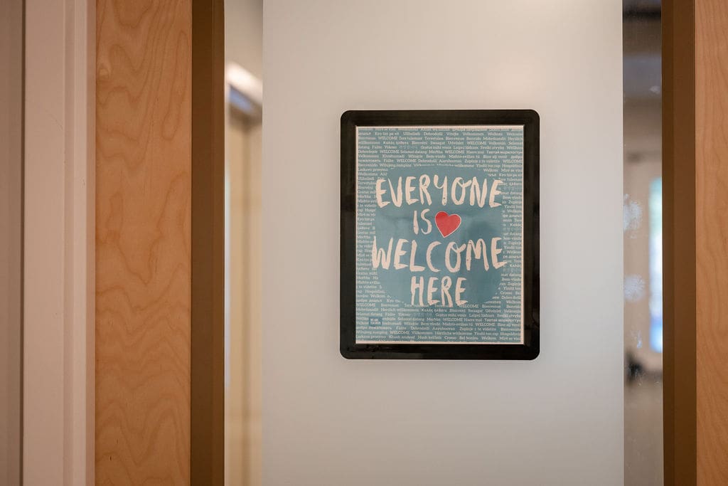 Framed sign on wall reads 'Everyone is welcome here' with a red heart.