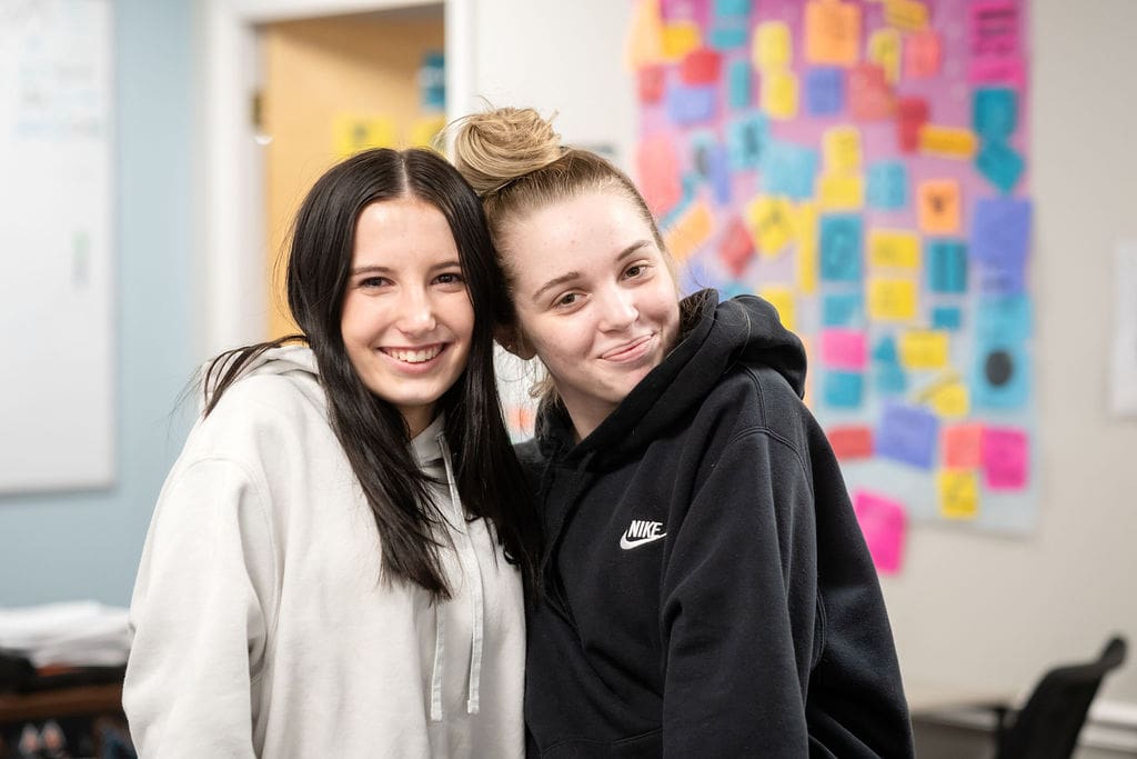 Two students standing close and smiling in a classroom.