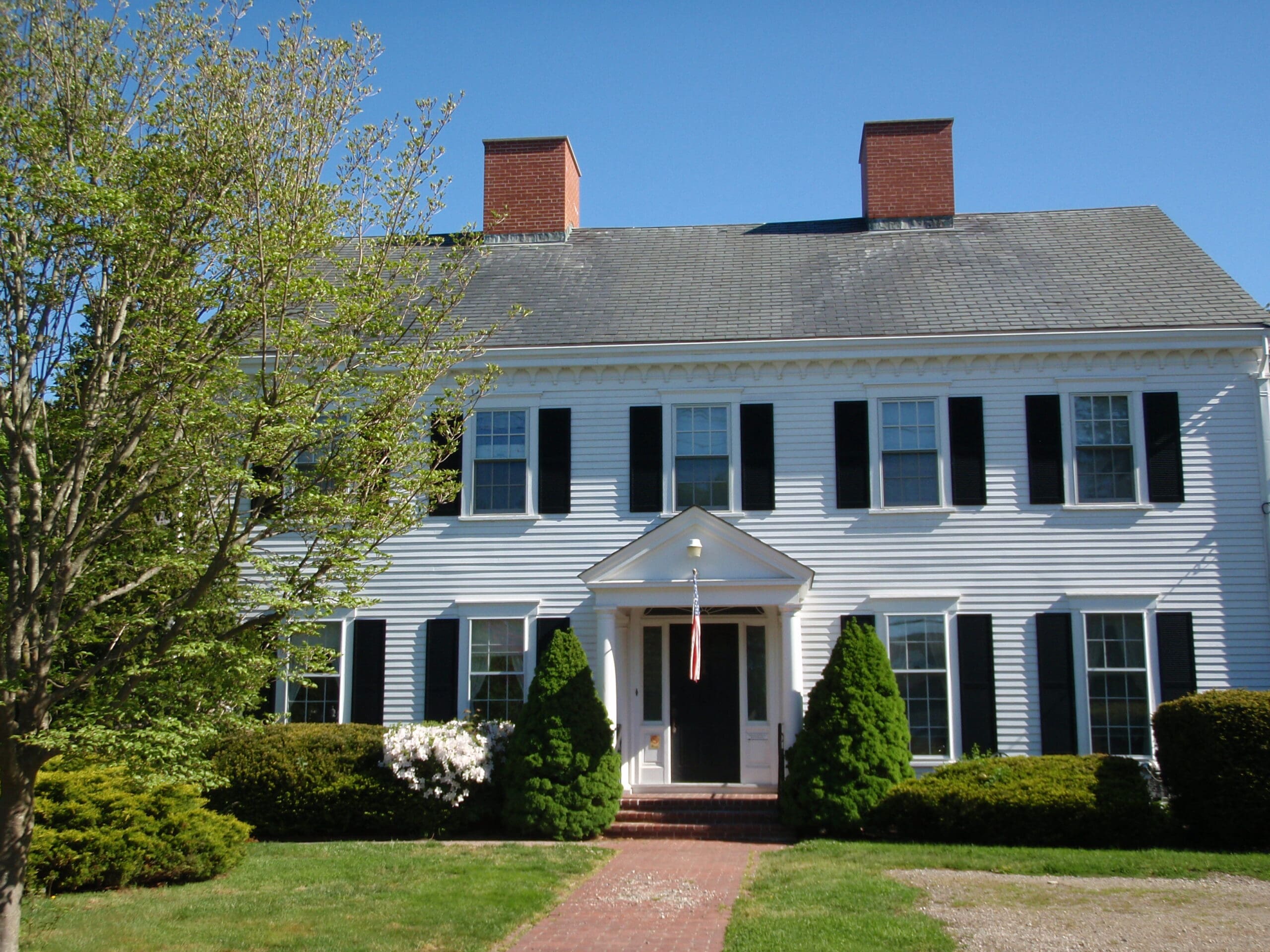 White house with black shutters, greenery, and a brick walkway