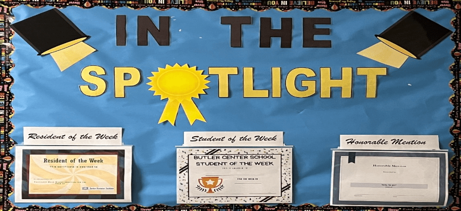 Three award certificates on a bulletin board with a blue background and school-themed decorations.