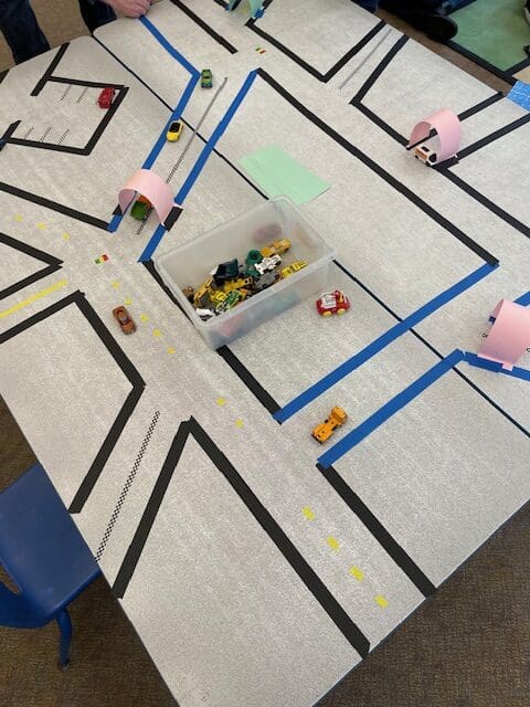 Toy cars on a play mat with roads, traffic cones, and tunnels.
