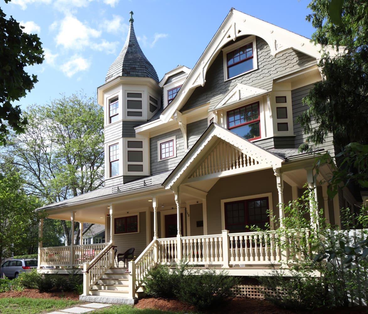 Victorian-style house with a front porch, surrounded by greenery.