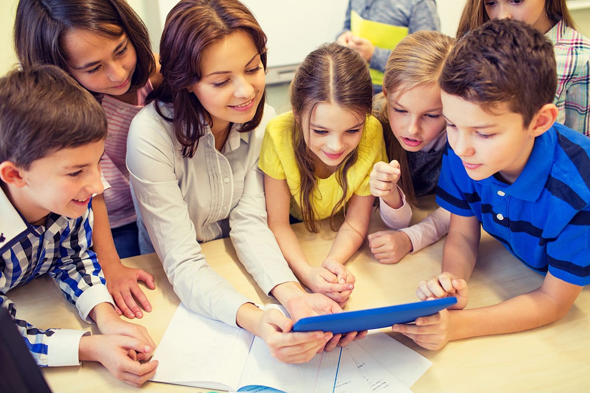 Group of children and adult looking at a tablet together on a table.