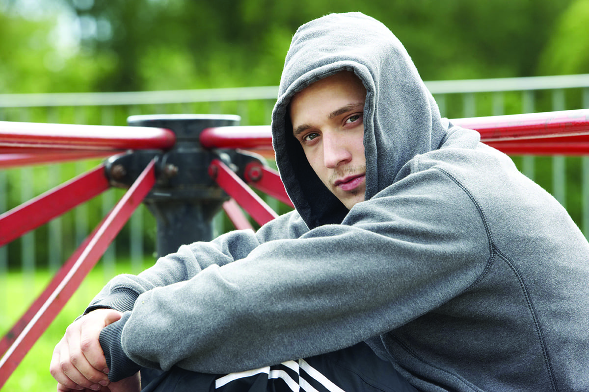Young person in a gray hoodie sitting outdoors, looking serious.