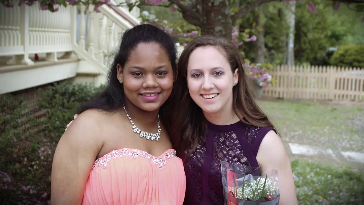 Two smiling individuals outdoors, one holding a bouquet of flowers.