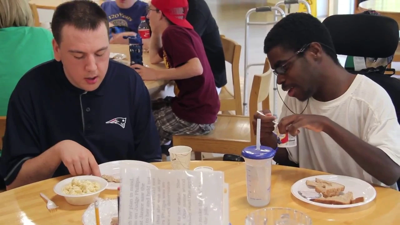 Two individuals sitting at a table, eating and engaging in conversation