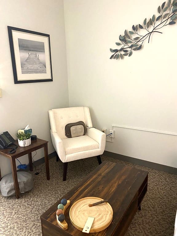 Empty sitting room with a white armchair, wooden table, and wall art.