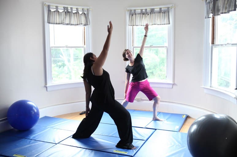 Two people practicing yoga on blue mats in a bright room.