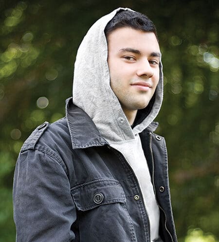 Person in hoodie and jacket outdoors, looking at camera