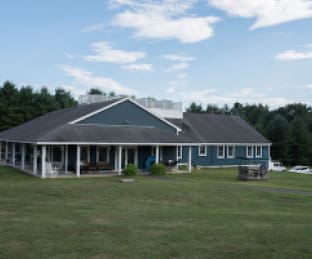 Single-story building with a porch and blue walls, surrounded by grass.