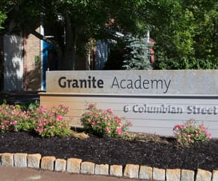 Sign reading Granite Academy at 6 Columbian Street, surrounded by flowers.