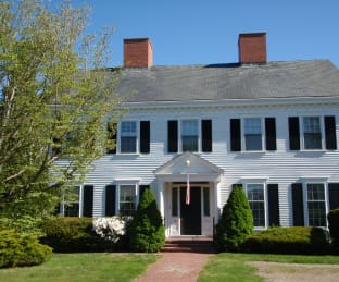 Image of a large, white, two-story house with black shutters and a front porch.