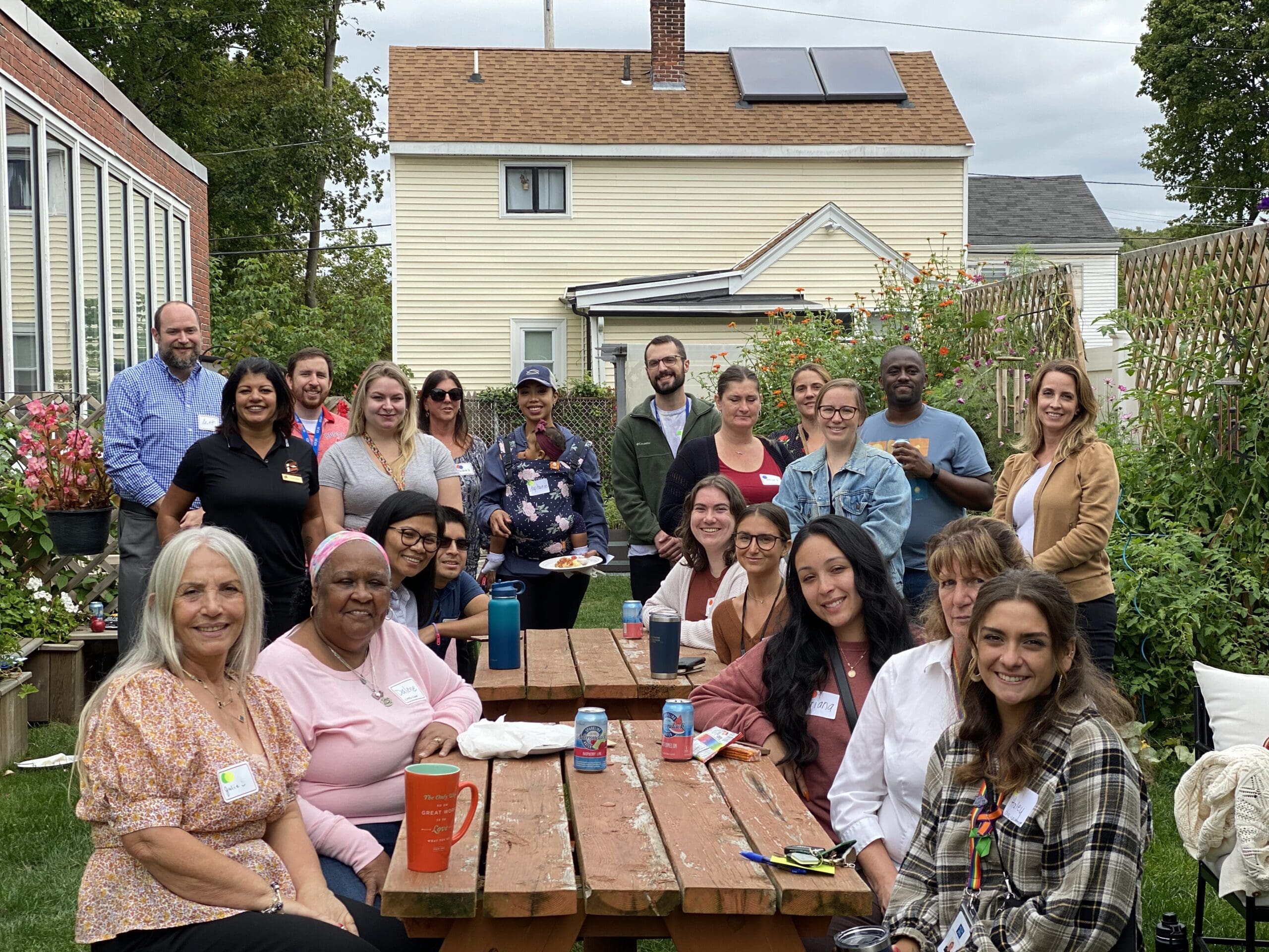 Group of diverse people smiling, gathered outdoors around a table.