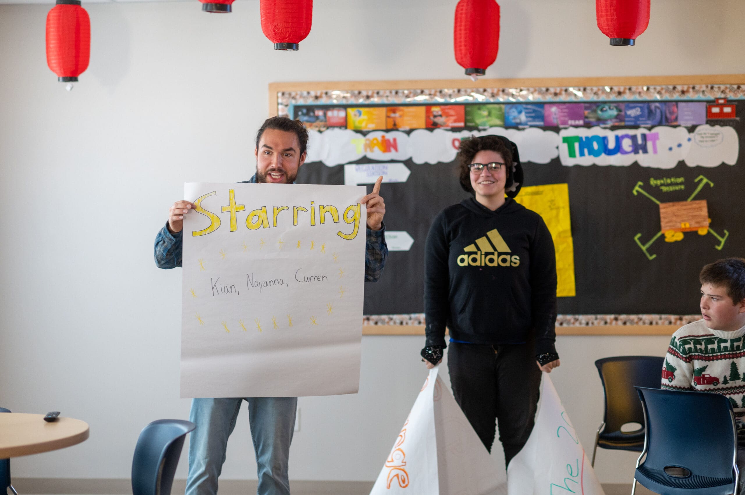 Two people holding signs in a classroom, smiling.