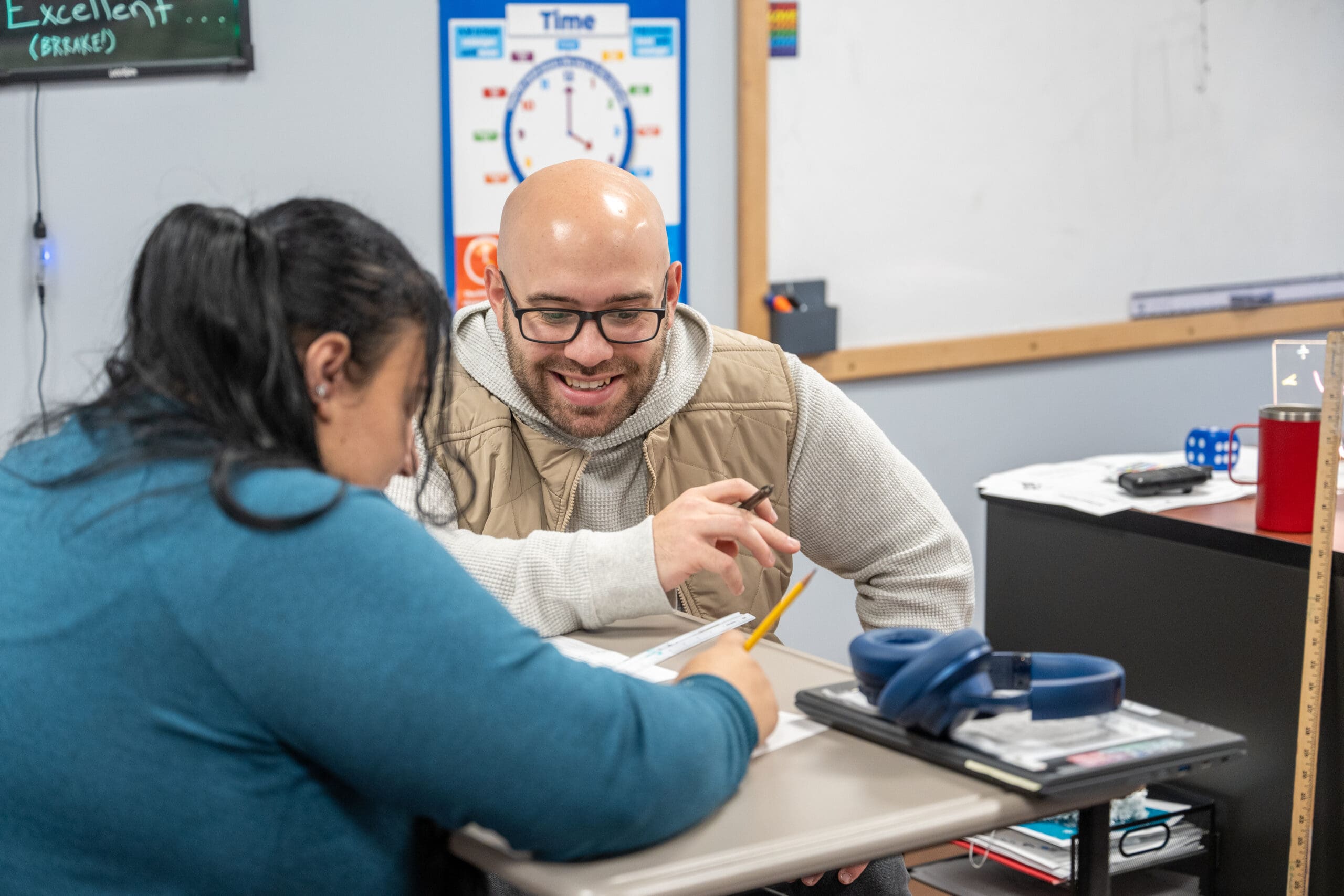 Teacher assisting a student with a worksheet in the classroom.