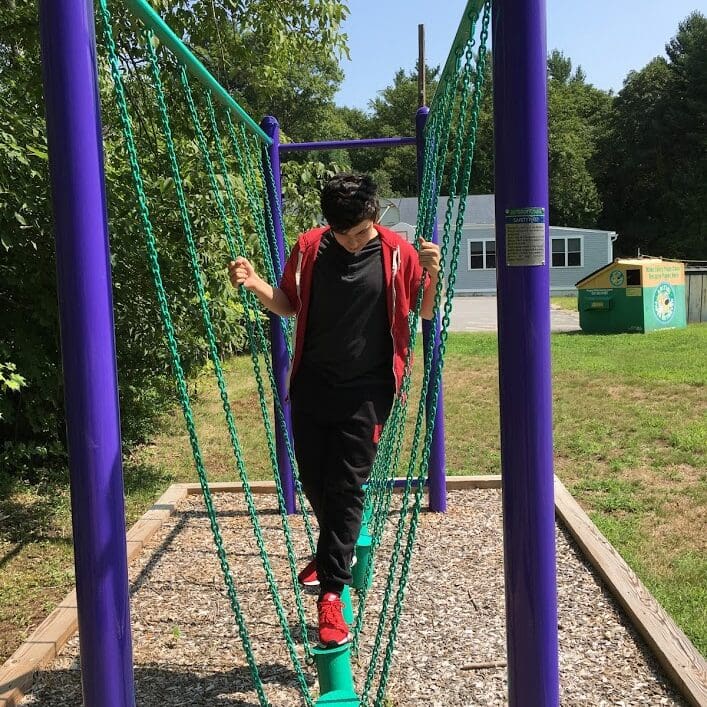 Person walking on a balance beam in a playground with chains and purple supports
