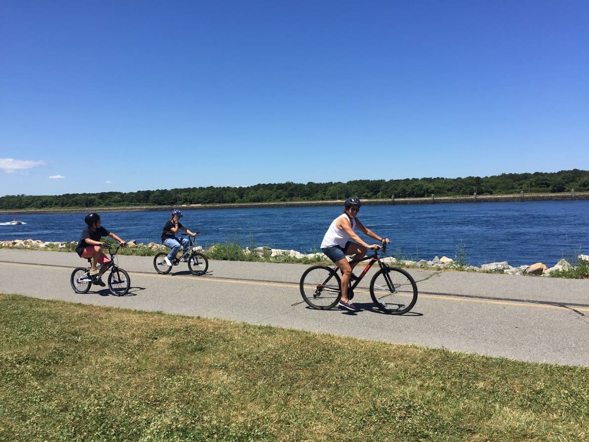 Adult and two children riding bikes along a waterfront path.