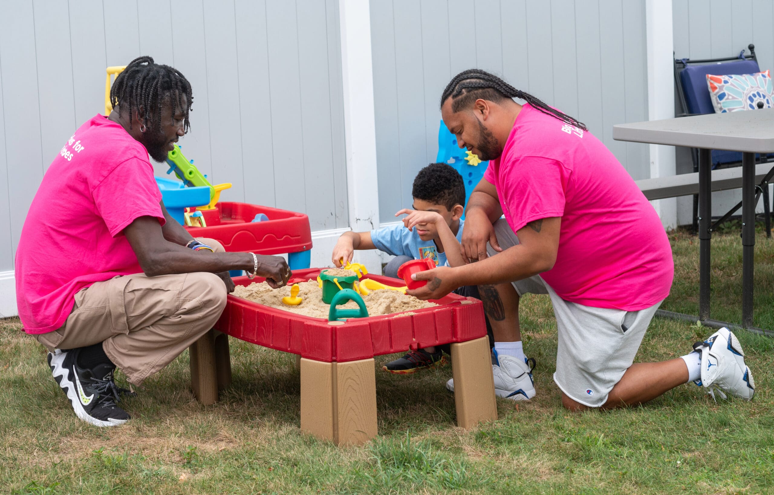 Two adults and a child playing in a sandbox outside.