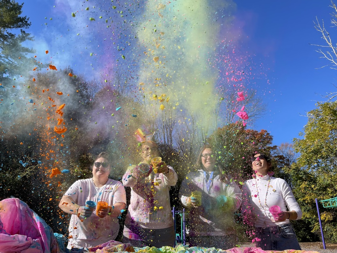 Four people throwing colored powder into the air outdoors.