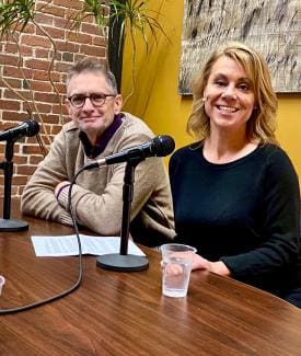 Two people smiling at a table with microphones.