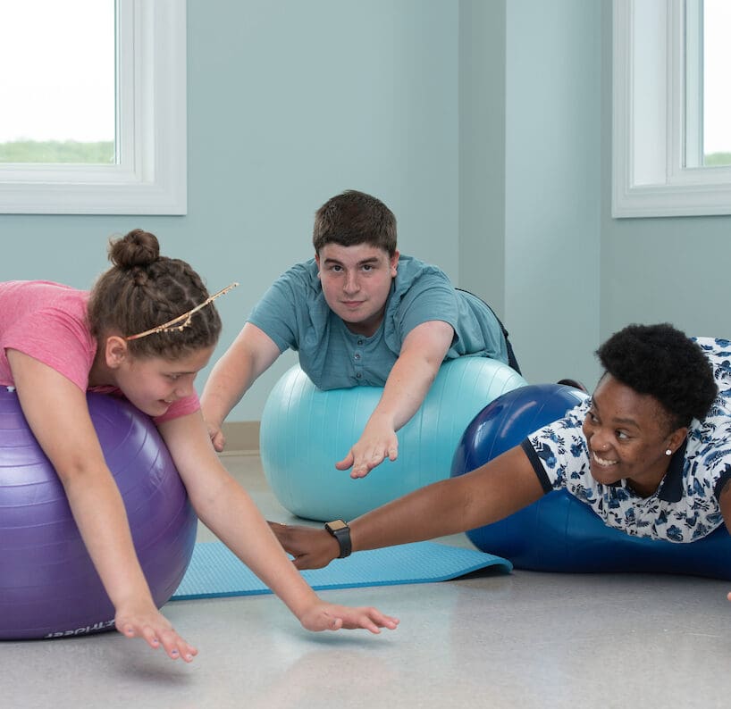 Three individuals doing a stretching exercise with exercise balls.