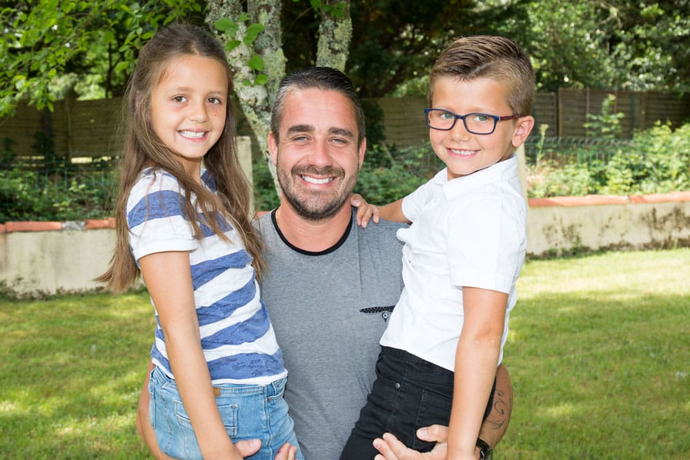 Man with two children outdoors, smiling.