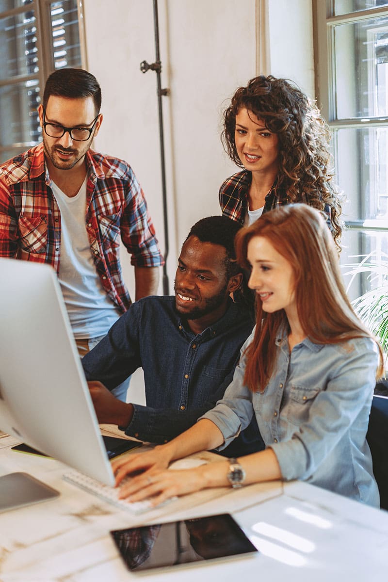 Four people gather around a computer, looking engaged.
