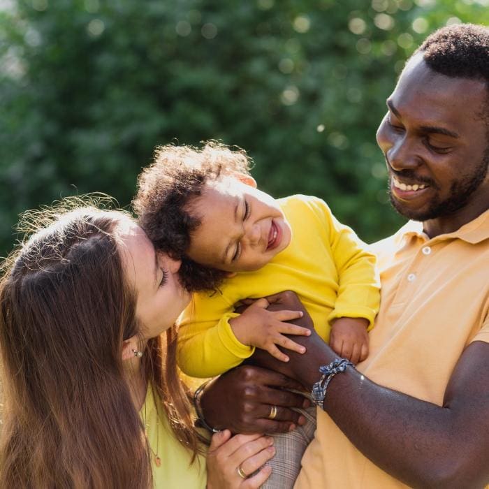 Man holding laughing toddler, woman leaning in with her face close to the child.