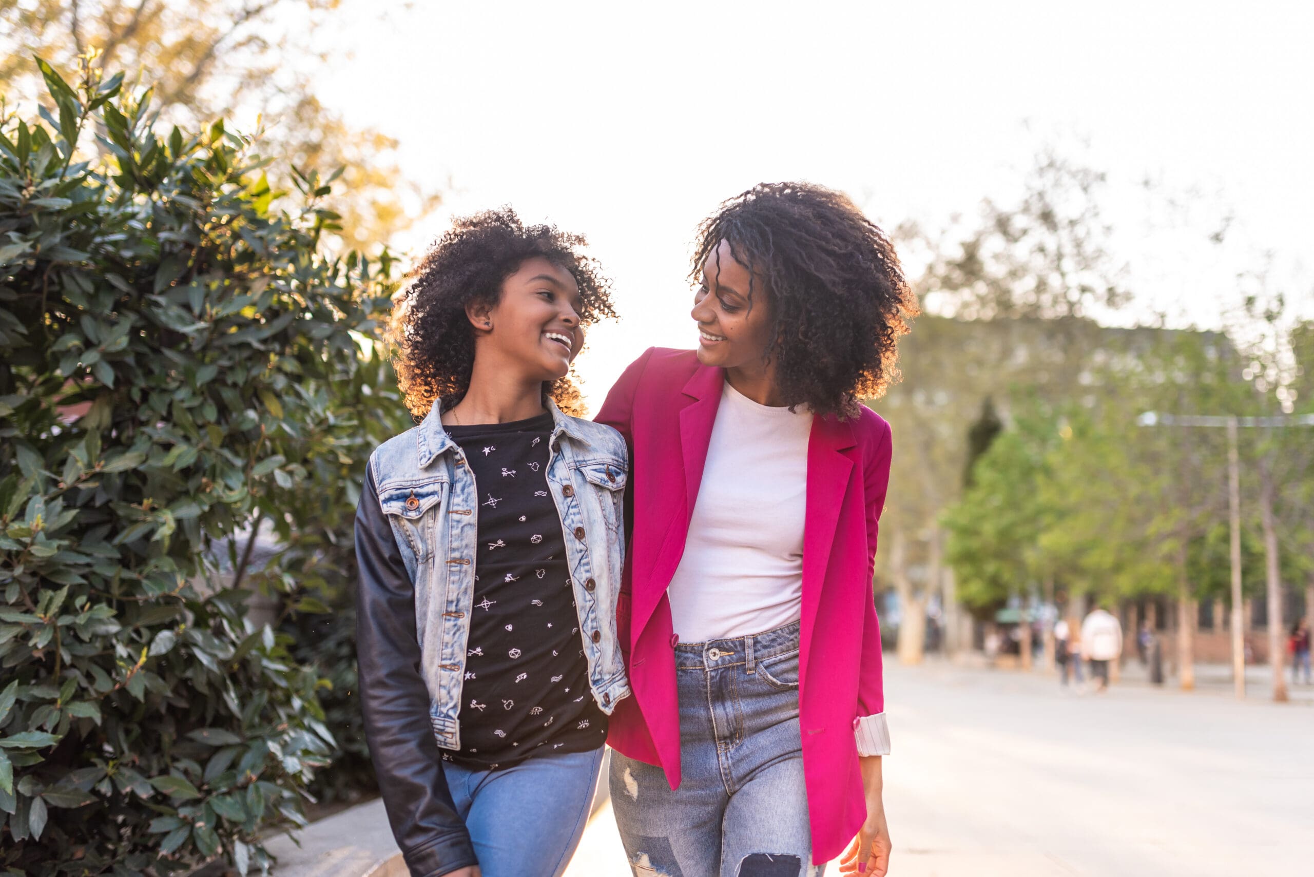 Mother and teenage daughter walking and smiling together outdoors.