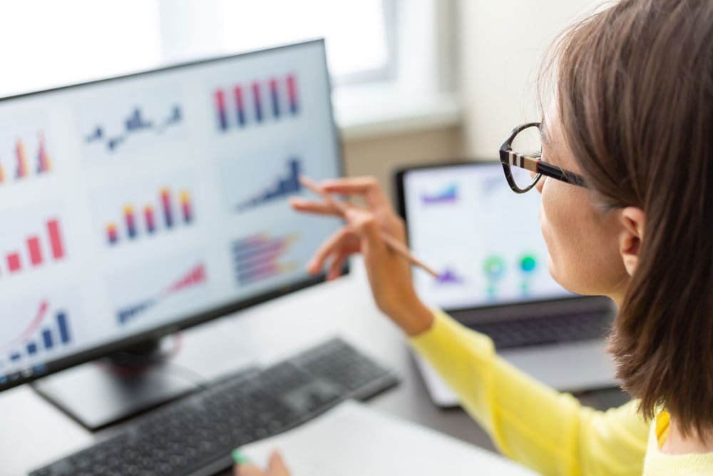 Person pointing at colorful bar graphs on a computer monitor.