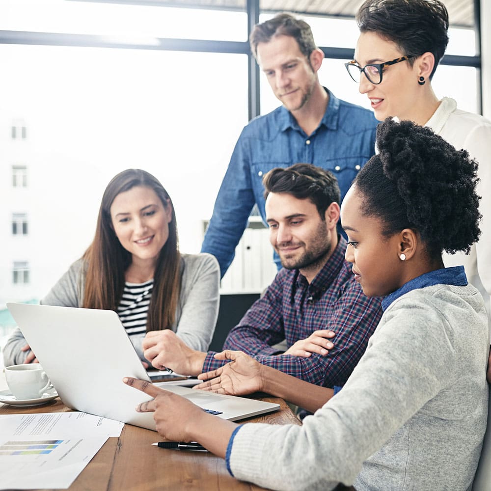 Group of five people collaborating around a laptop in an office.