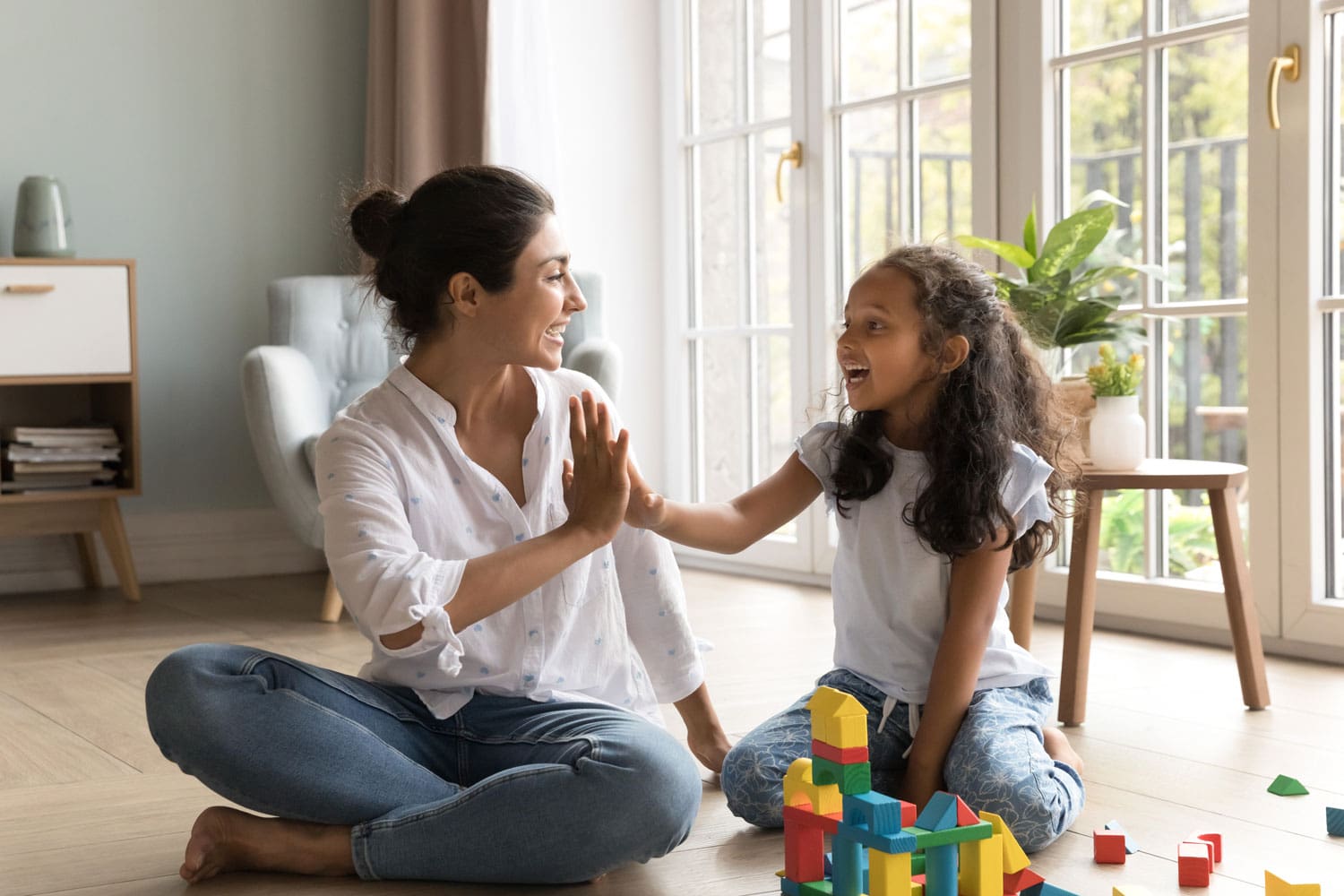 Mother and daughter playing with building blocks, smiling, in bright room.